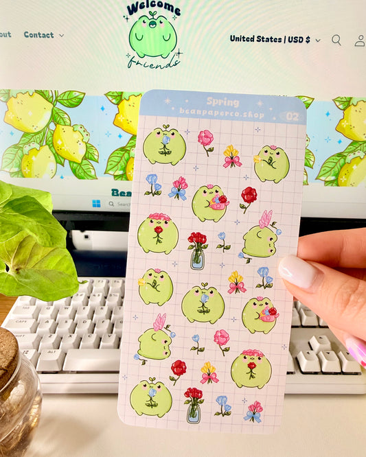 Hand holding Kawaii Spring Planner Stickers of frog characters and flowers.