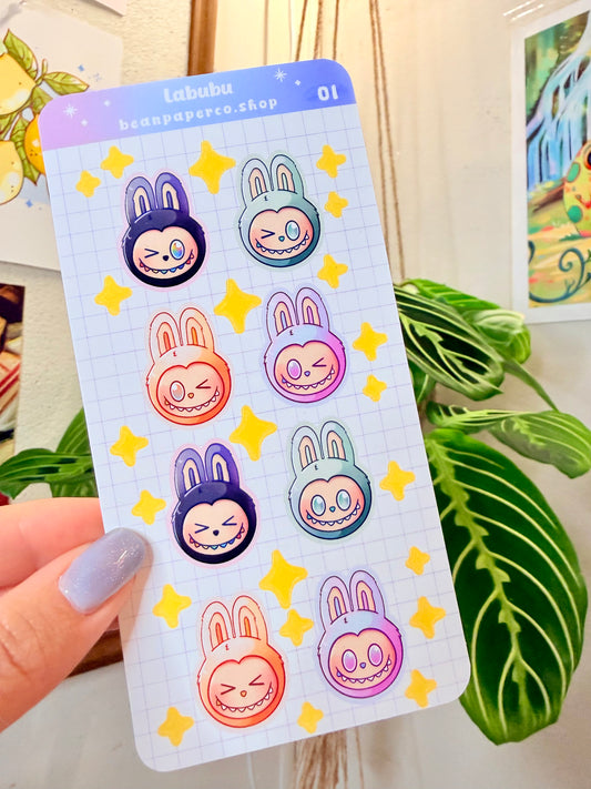 Labubu The Monster Sticker Sheet with black, blue green, orange, and purple labubus held by hand with plant in the background.