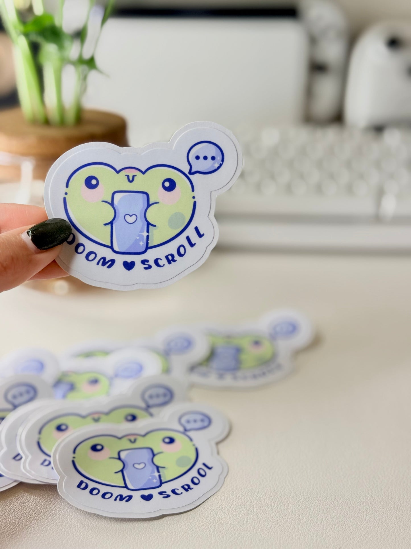 “Cute frog sticker holding a phone with the words ‘Doom Scroll’ underneath and a speech bubble above.”