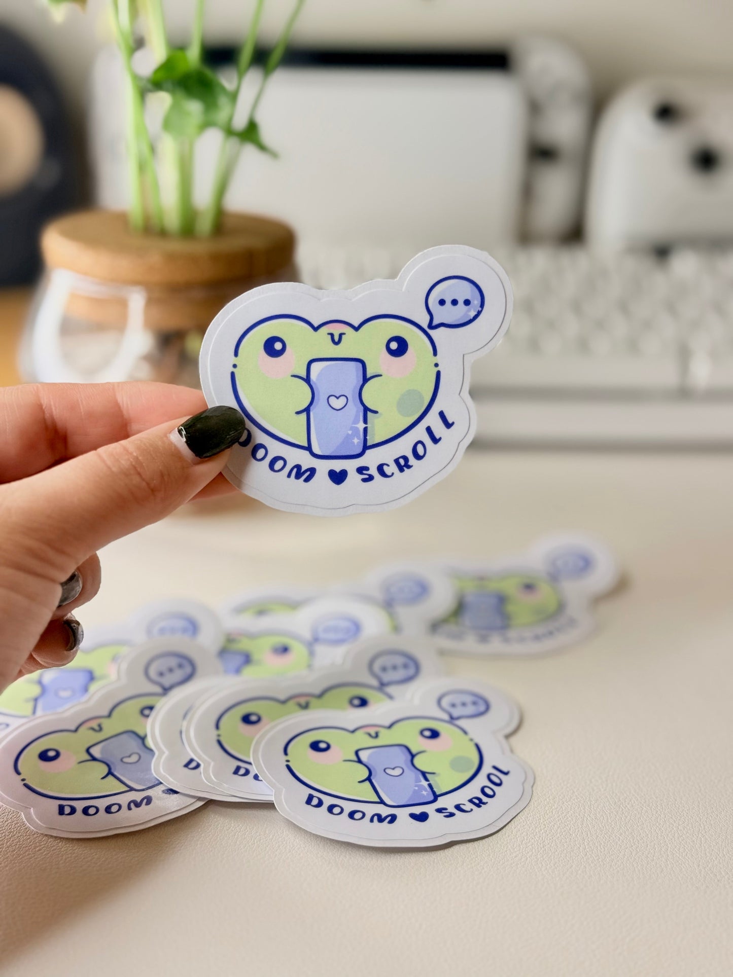 “Cute frog sticker holding a phone with the words ‘Doom Scroll’ underneath and a speech bubble above.”