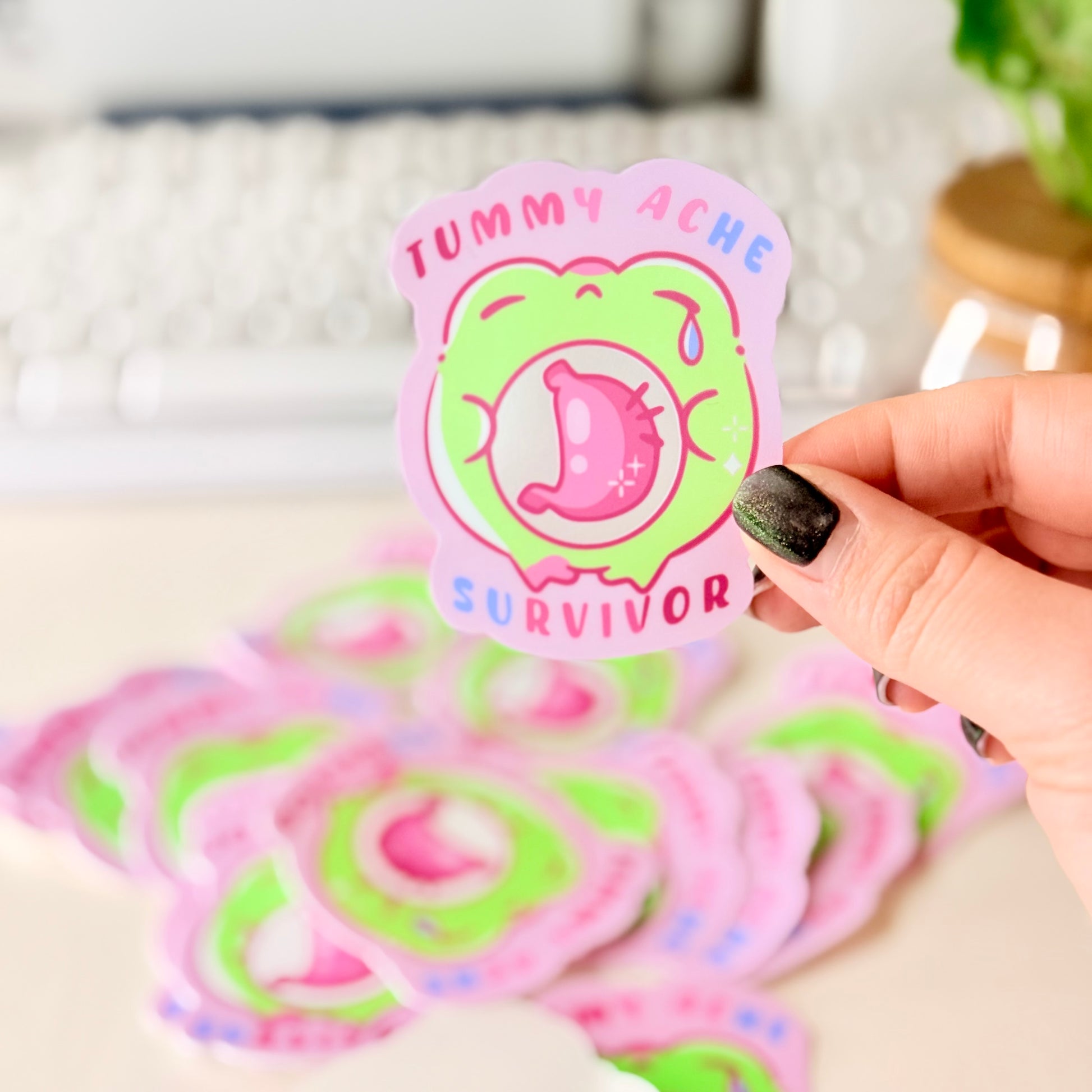 Tummy Ache Survivor Frog Sticker featuring Pastel pink and green frog sticker reading "Tummy Ache Survivor’ with a crying frog holding its stomach".