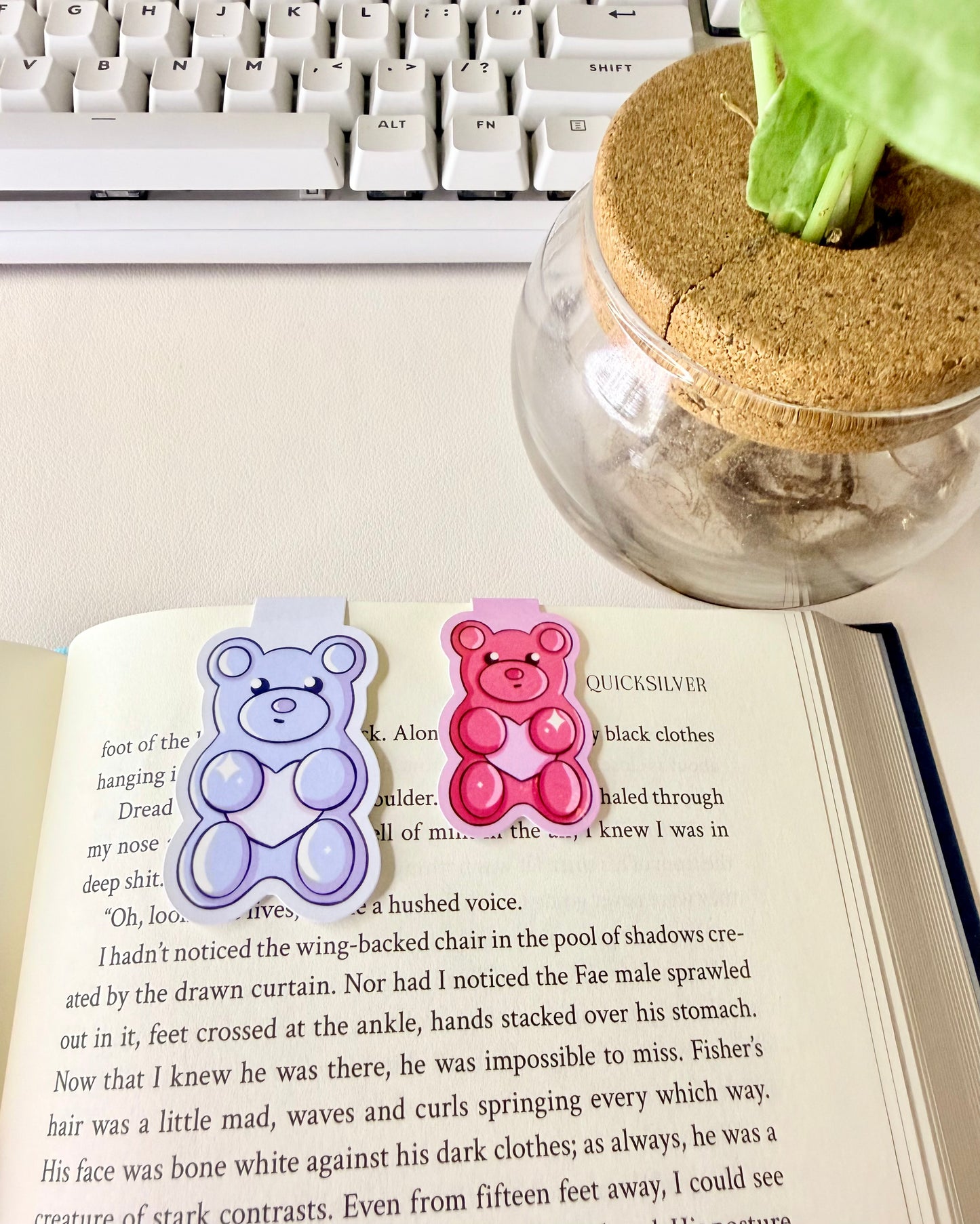 "Blue and Hot pink gummy bear magnetic bookmark set in book showcasing how it can be used as well as the size difference. Blue bookmark is larger while the pink bookmark is smaller."