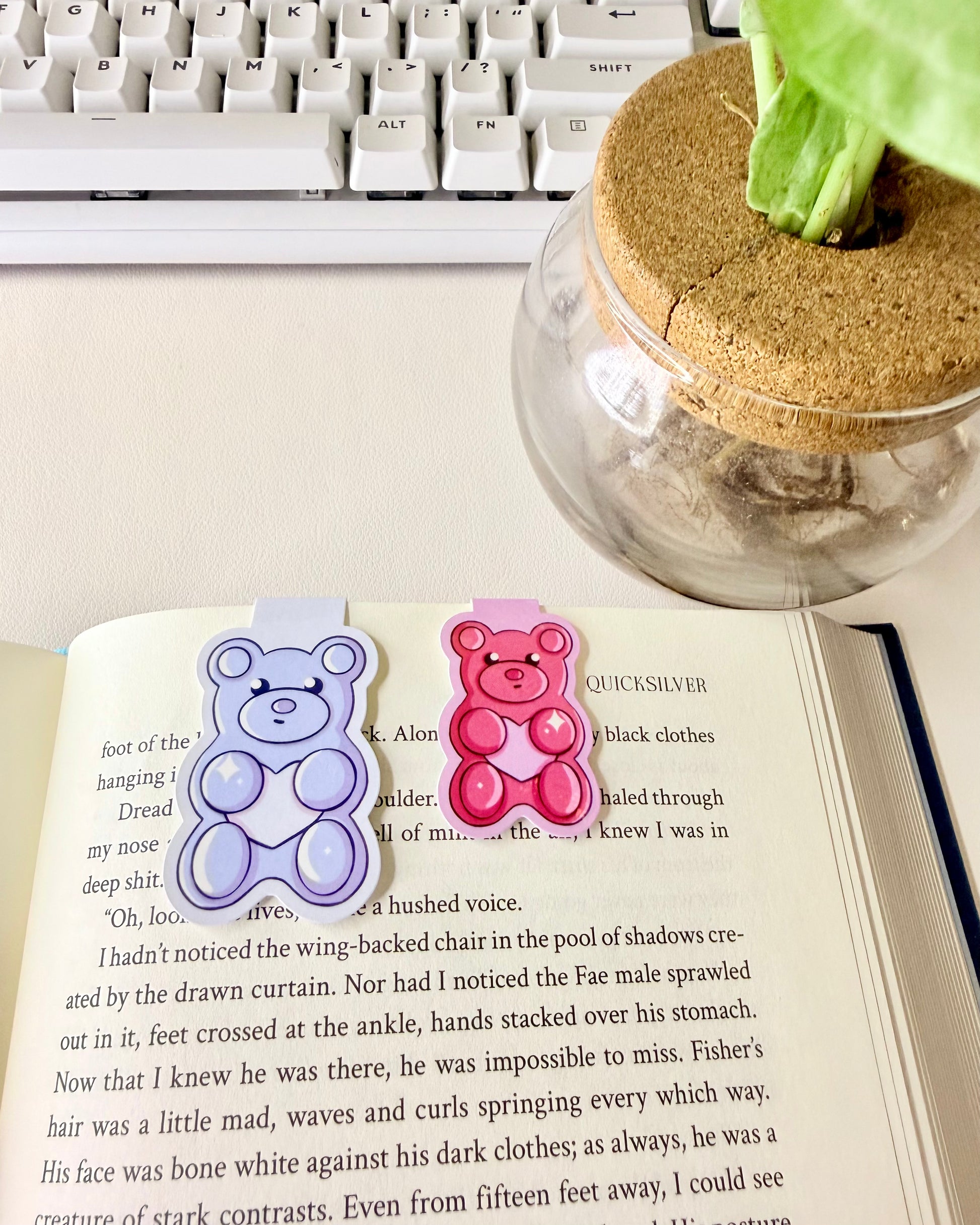 "Blue and Hot pink gummy bear magnetic bookmark set in book showcasing how it can be used as well as the size difference. Blue bookmark is larger while the pink bookmark is smaller."