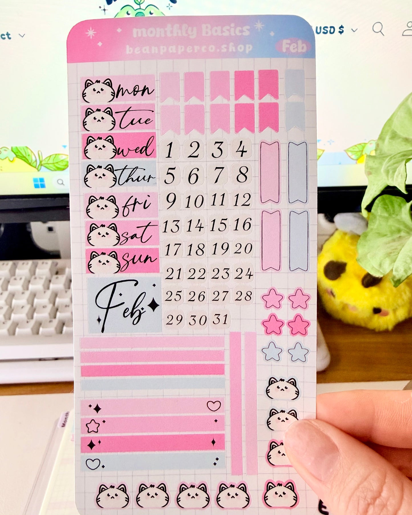 Hobonichi Weeks February Functional Monthly Planner Kitt featuring pink and blue date covers, weekday labels with cute cat faces, number stickers, star icons, and decorative boxes.