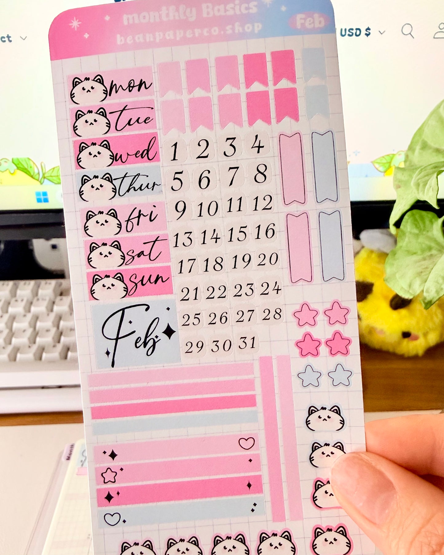 Hobonichi Weeks February Functional Monthly Planner Kitt featuring pink and blue date covers, weekday labels with cute cat faces, number stickers, star icons, and decorative boxes.