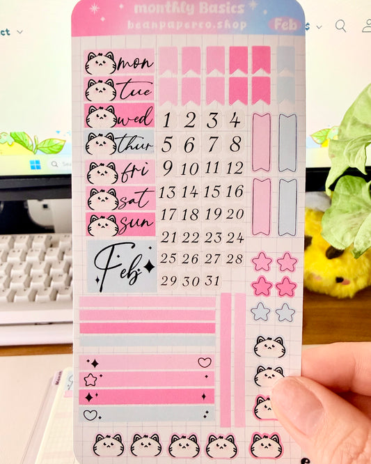Hobonichi Weeks February Functional Monthly Planner Kitt featuring pink and blue date covers, weekday labels with cute cat faces, number stickers, star icons, and decorative boxes.
