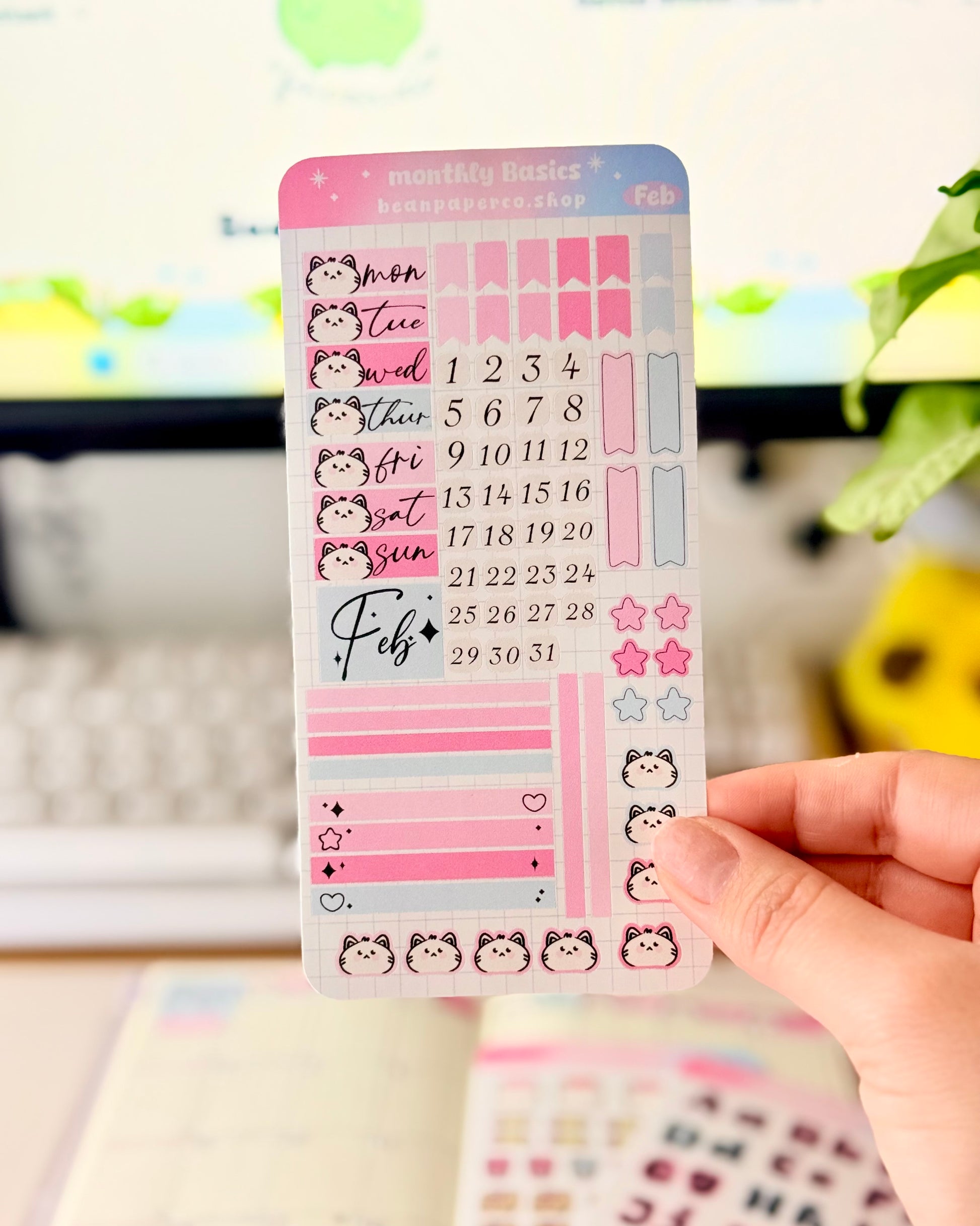 Hobonichi Weeks February Functional Monthly Planner Kitt featuring pink and blue date covers, weekday labels with cute cat faces, number stickers, star icons, and decorative boxes.