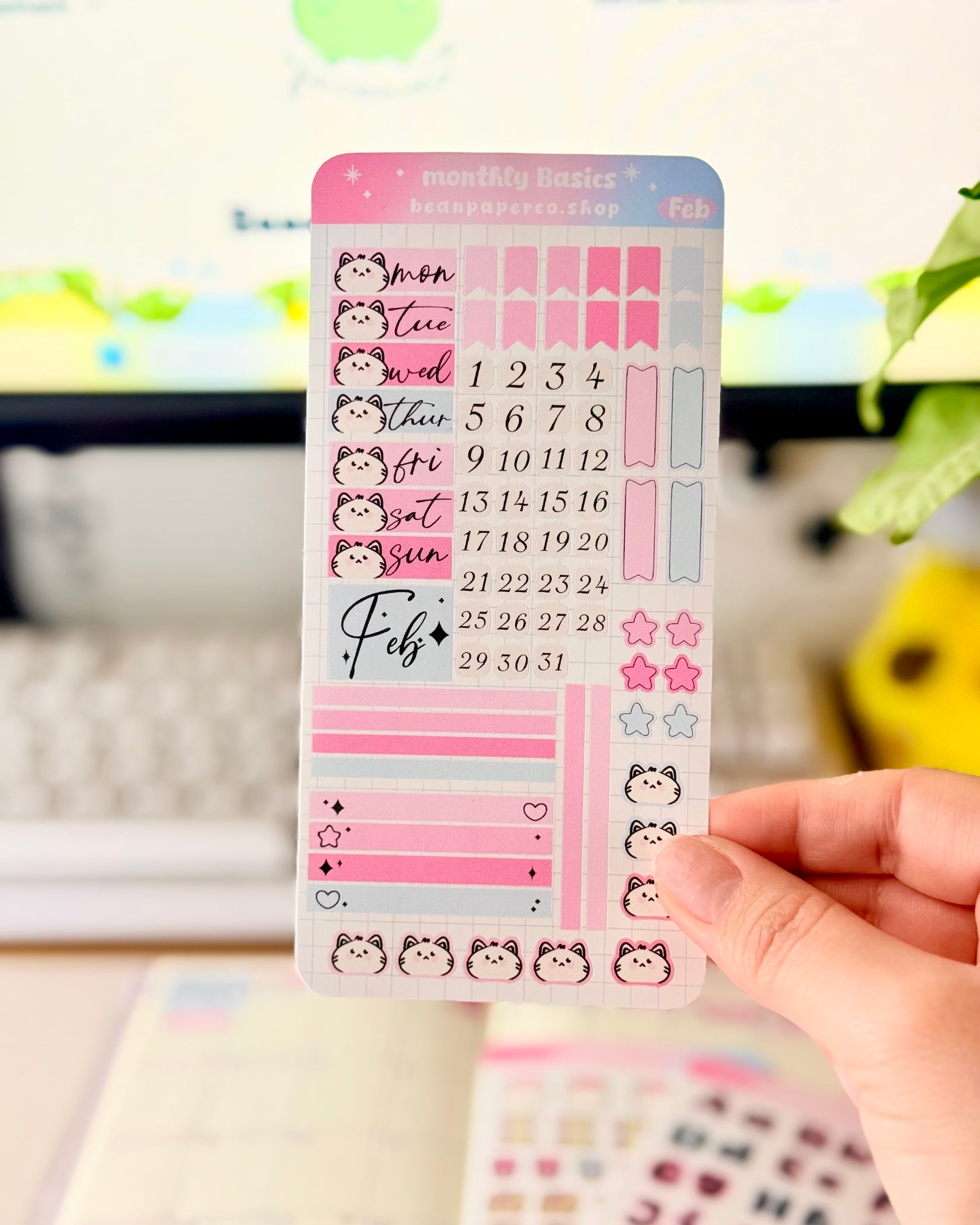 Hobonichi Weeks February Functional Monthly Planner Kitt featuring pink and blue date covers, weekday labels with cute cat faces, number stickers, star icons, and decorative boxes.