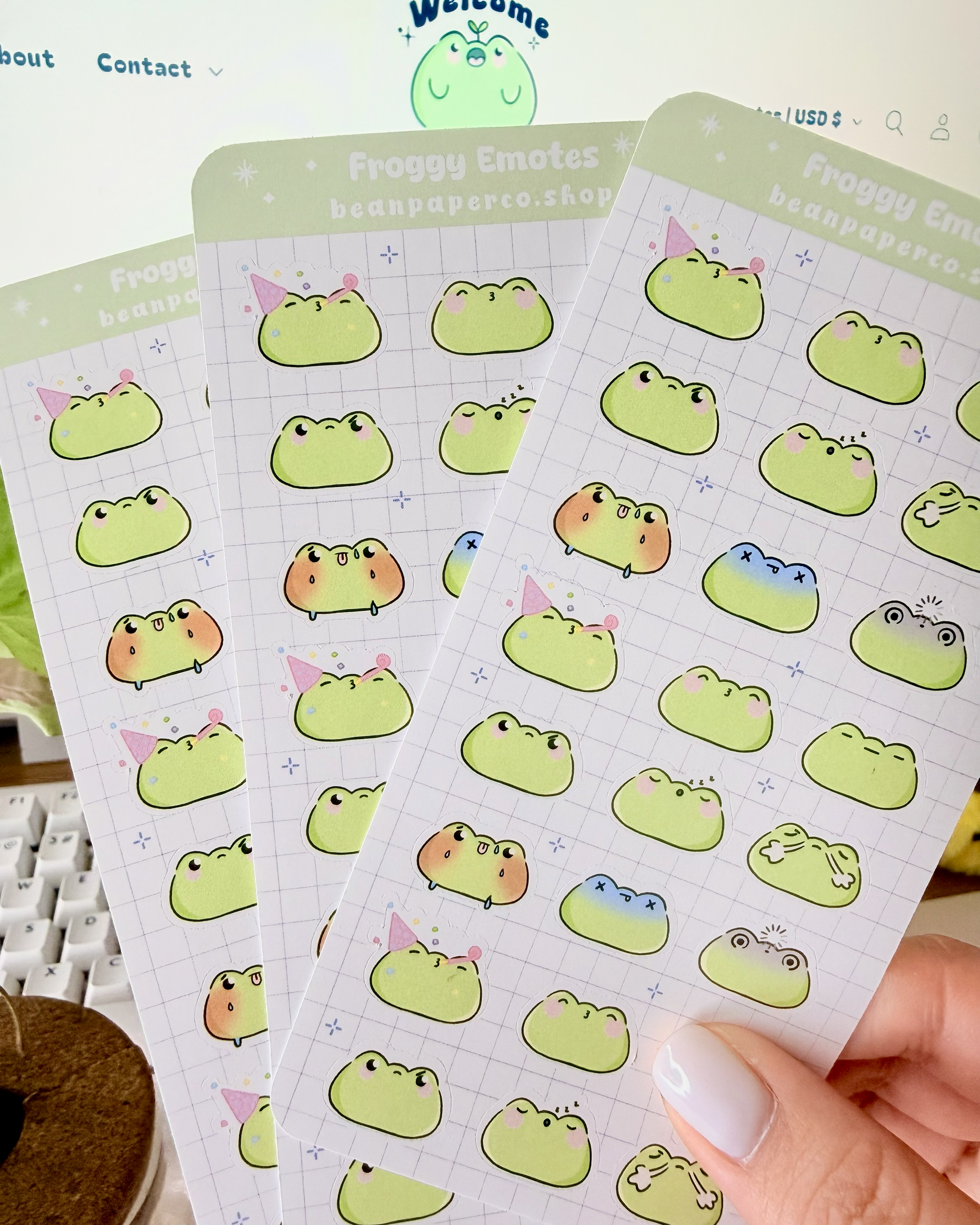 Cute Frog Emote Planner Stickers Vol. 2 featuring cute green frog faces with party hat, blushing, sleepy, angry, shocked, and fainting expressions on a light grid background.”