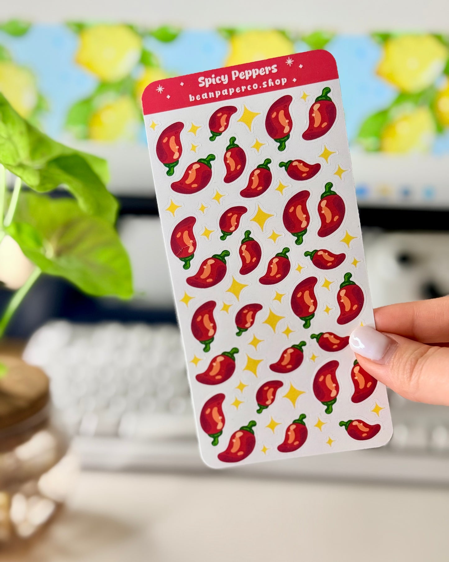 Cute Spicy Peppers Sticker Sheet held by a hand with a computer screen in the background.