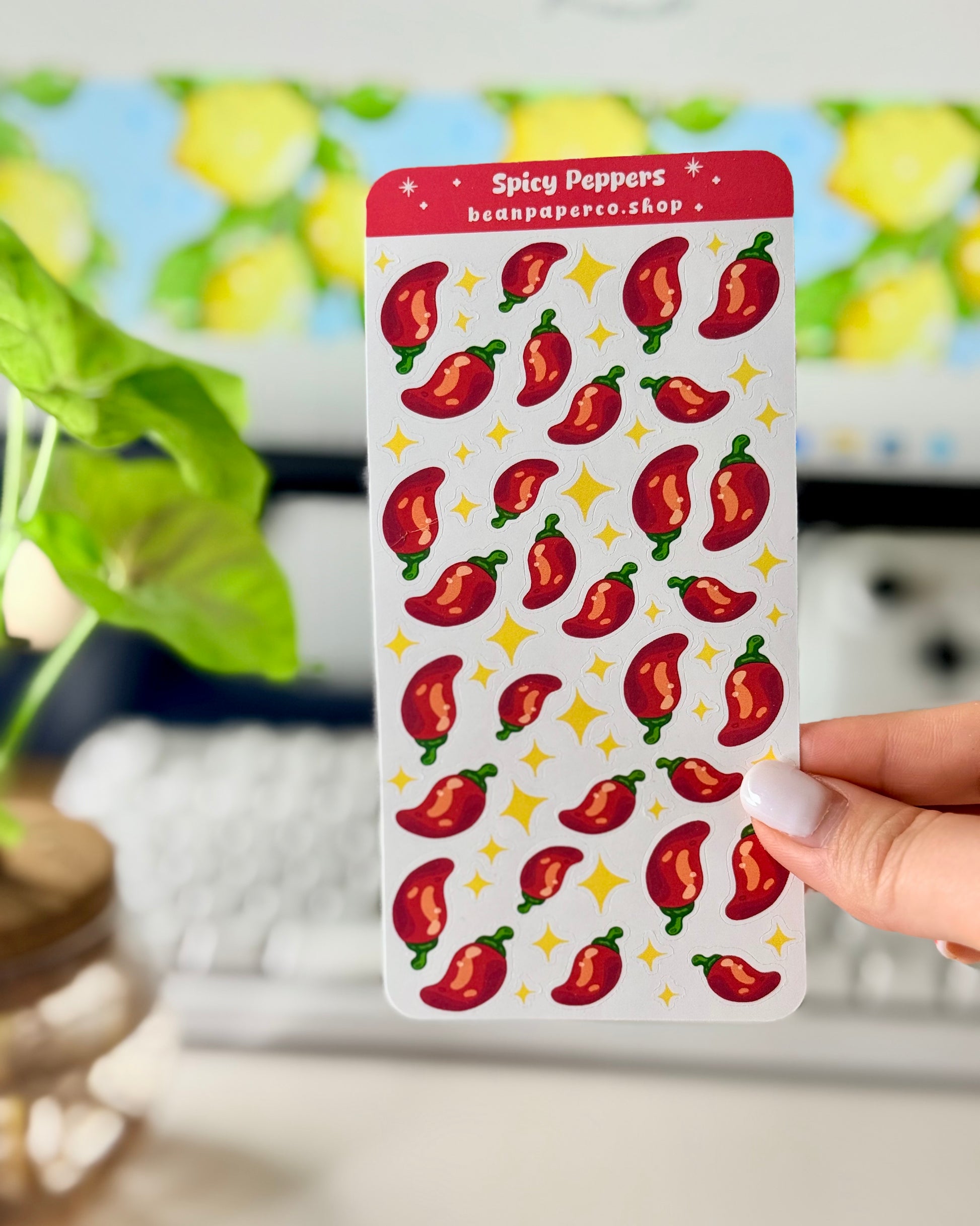 Cute Spicy Peppers Sticker Sheet held by a hand with a computer screen in the background.