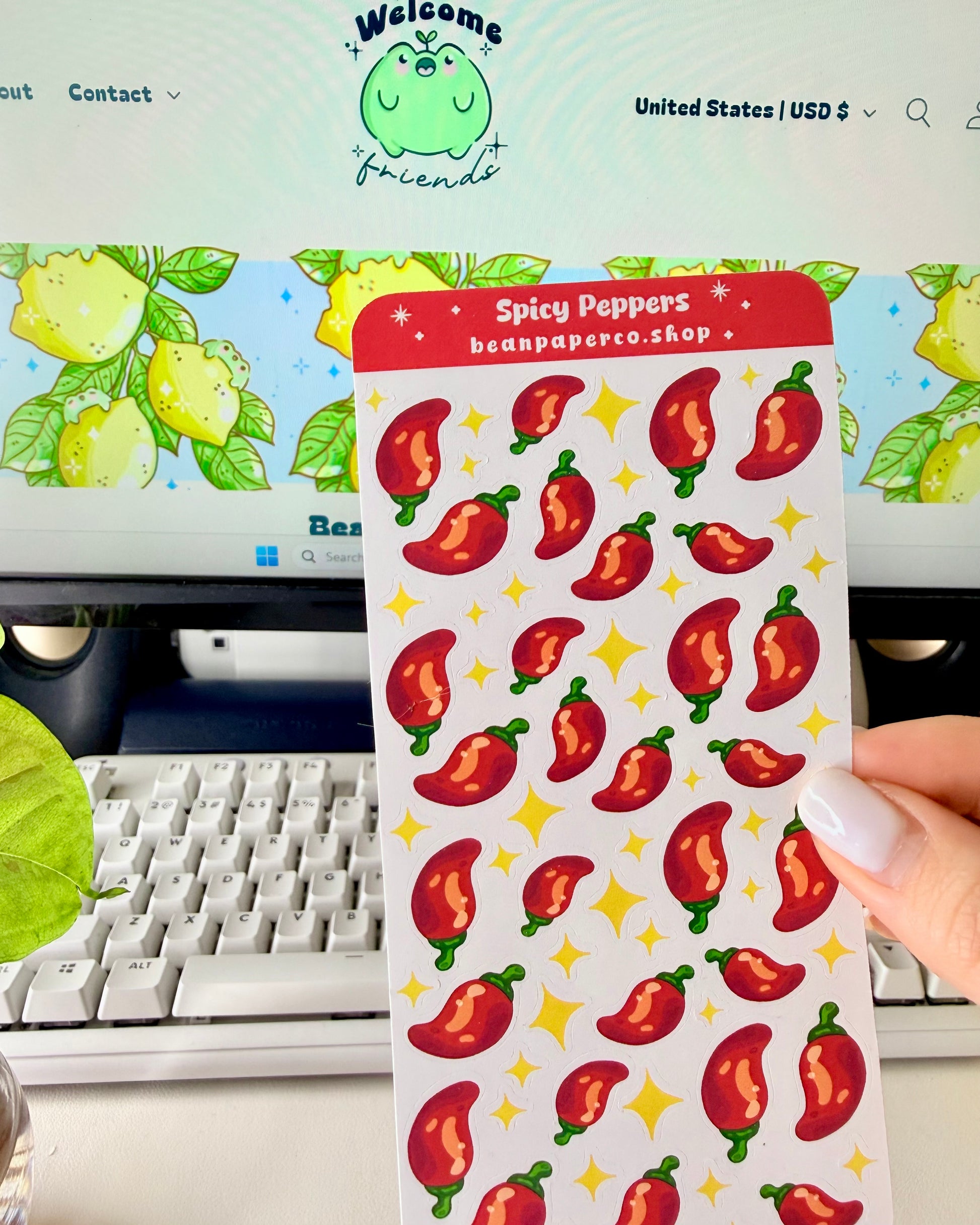 Cute Spicy Peppers Sticker Sheet held by a hand with a computer screen in the background.