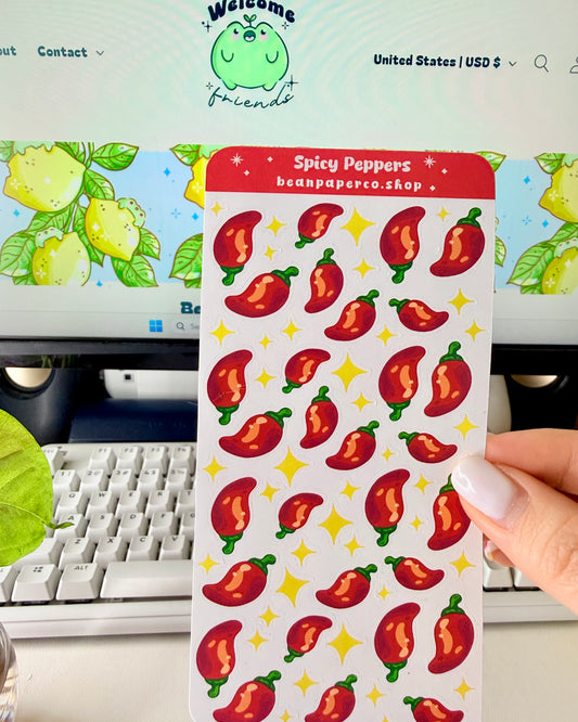 Cute Spicy Peppers Sticker Sheet held by a hand with a computer screen in the background.