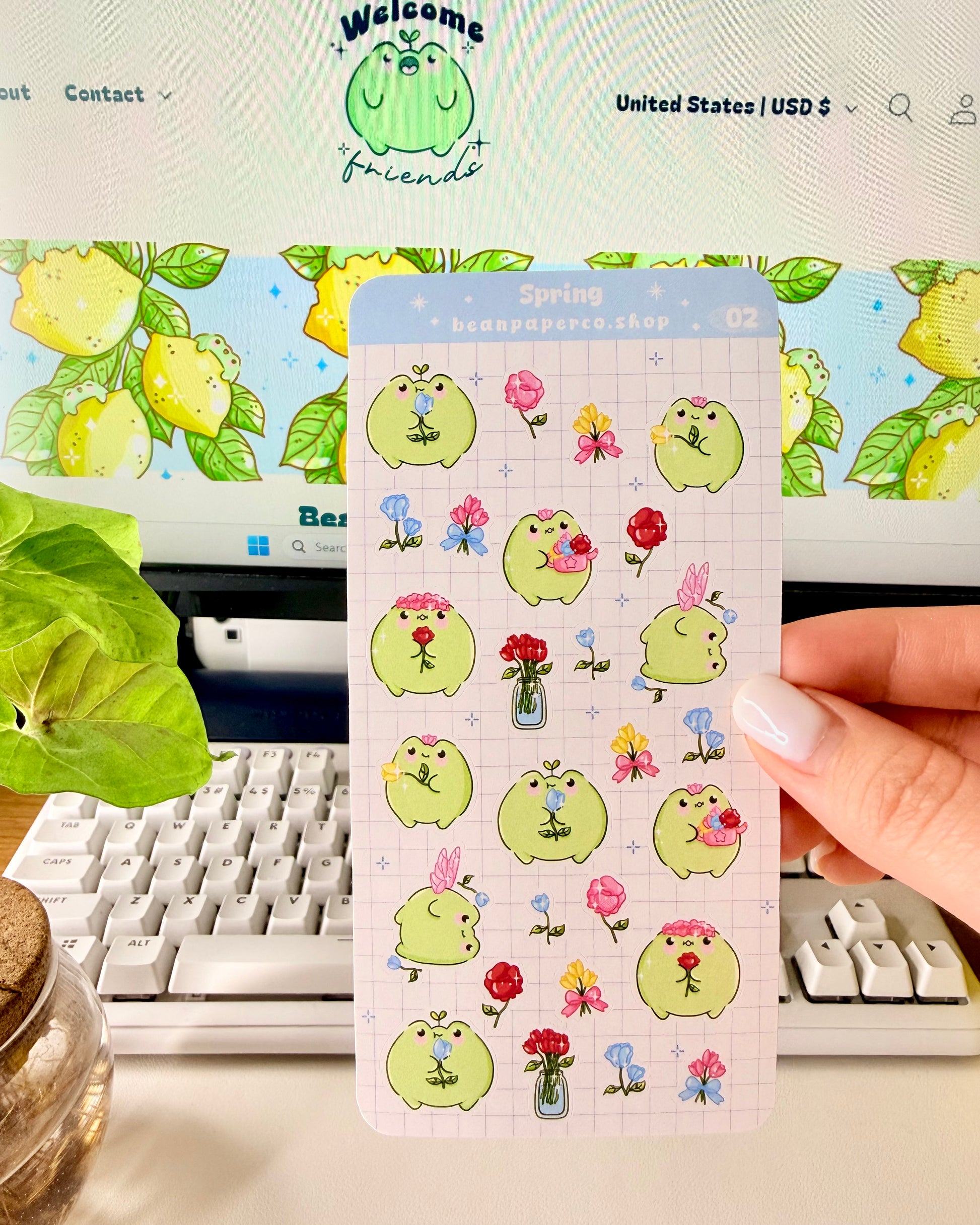Hand holding Kawaii Spring Planner Stickers of frog characters and flowers.