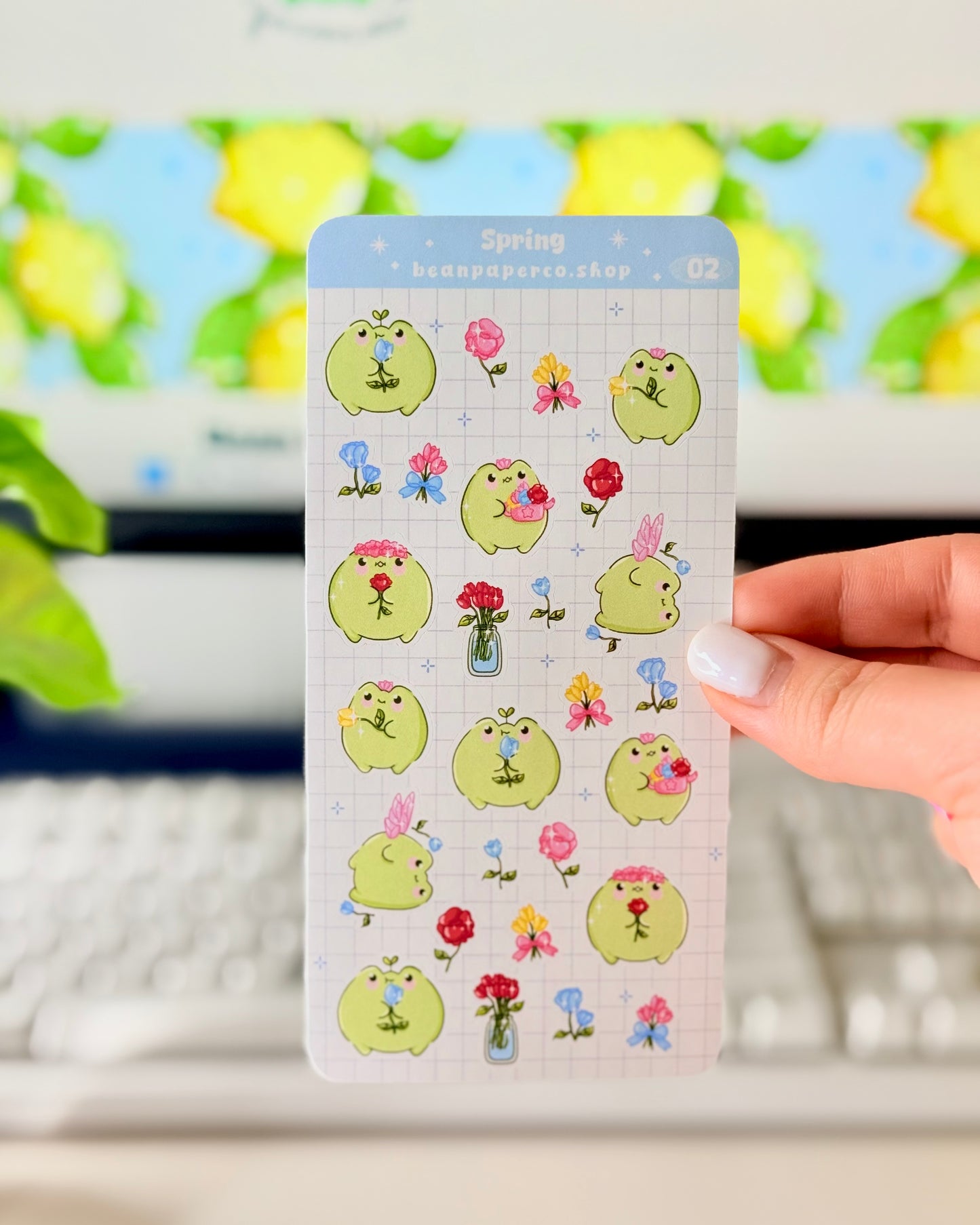 Hand holding Kawaii Spring Planner Stickers of frog characters and flowers.
