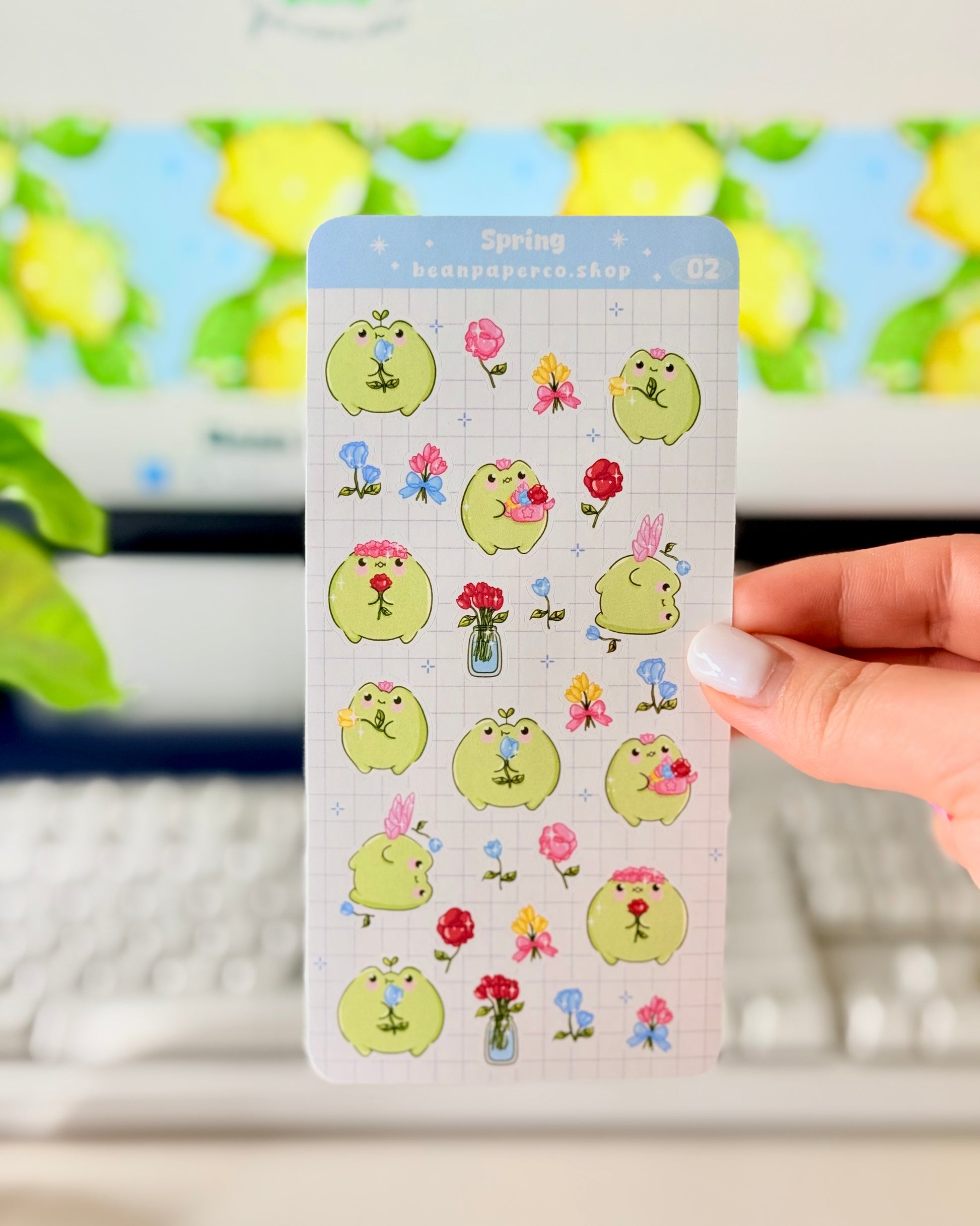 Hand holding Kawaii Spring Planner Stickers of frog characters and flowers.