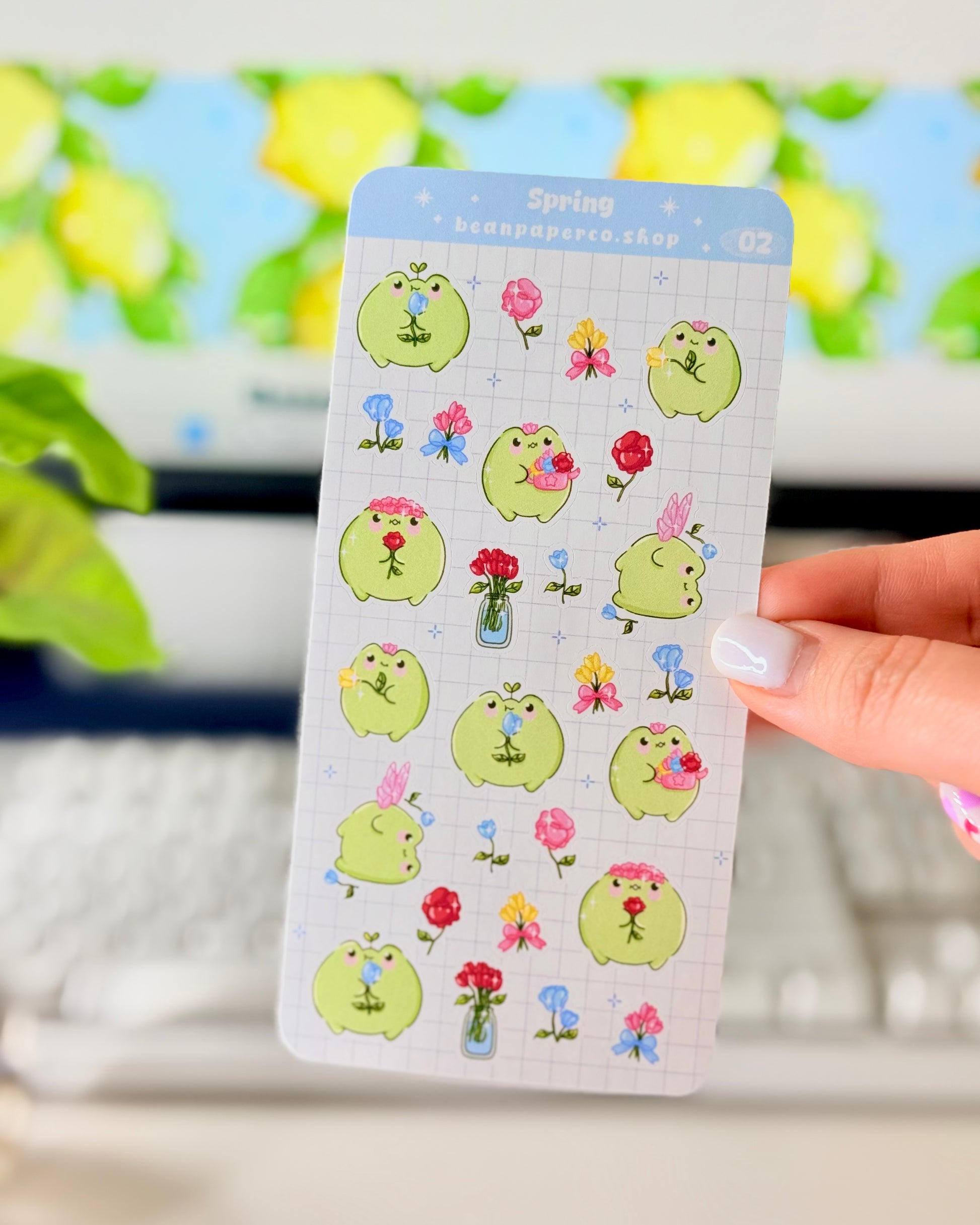 Hand holding Kawaii Spring Planner Stickers of frog characters and flowers.