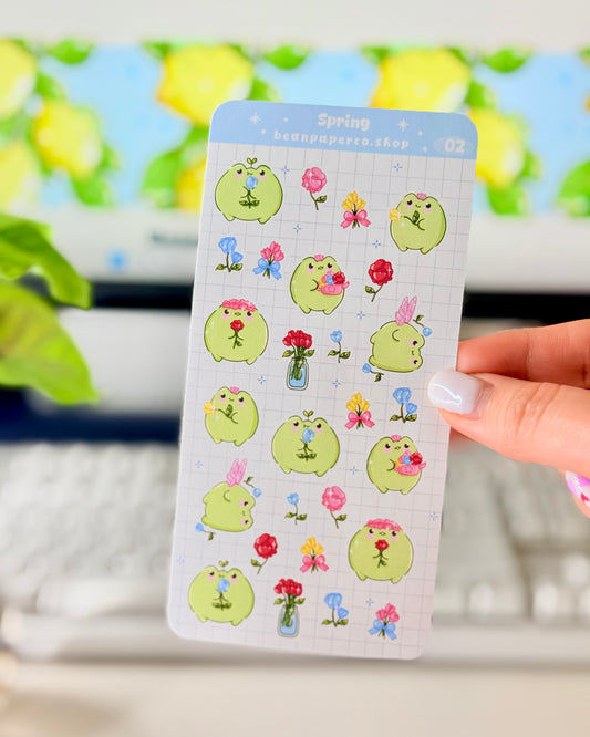 Hand holding Kawaii Spring Planner Stickers of frog characters and flowers.