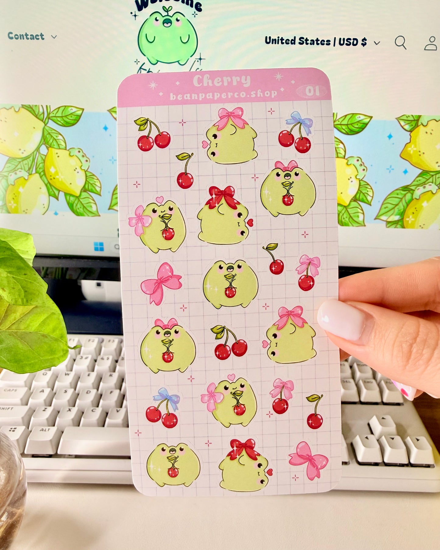 Hand holding a Cherry-themed frog sticker sheet featuring cute green frogs with pink bows, and red cherries.