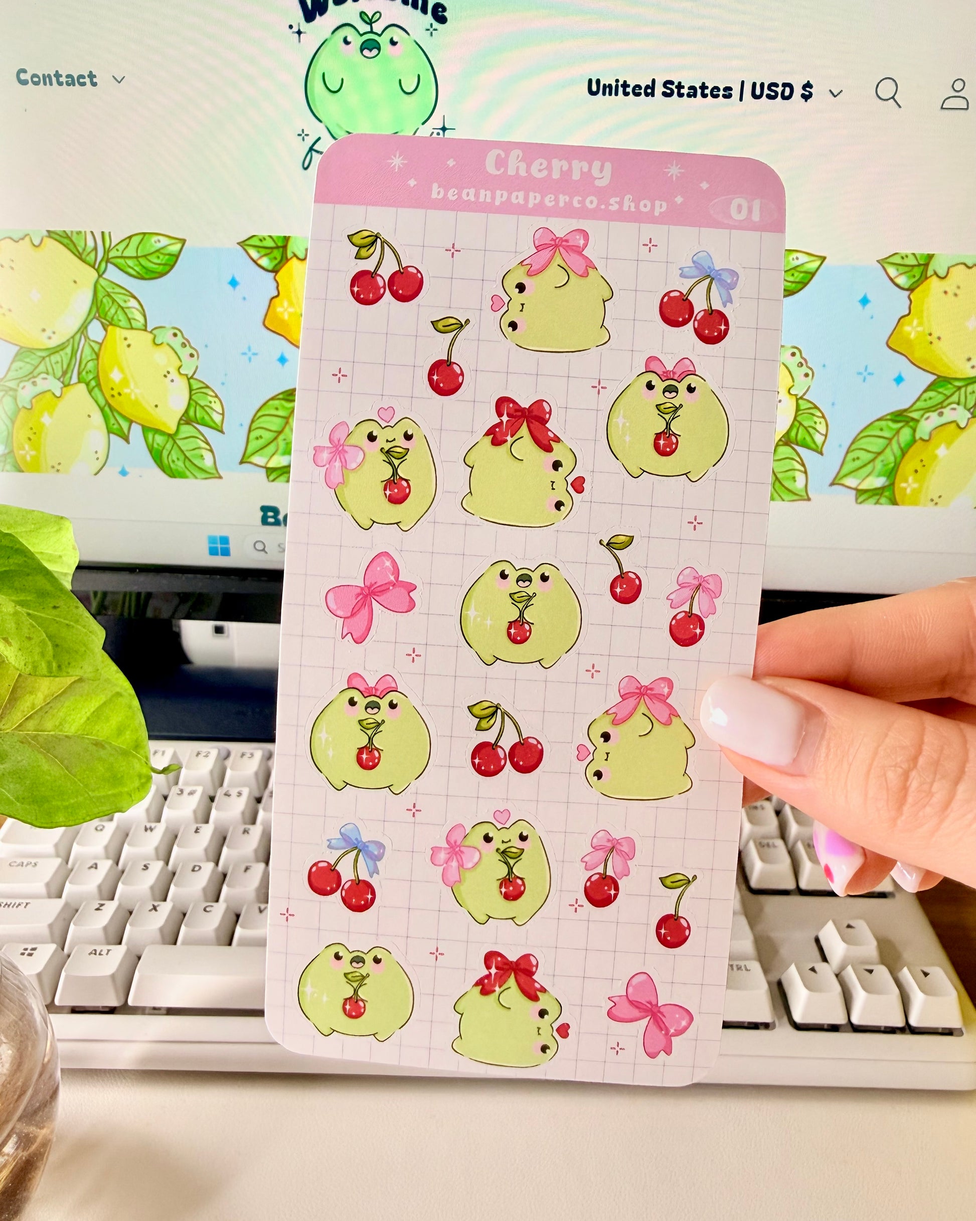 Hand holding a Cherry-themed frog sticker sheet featuring cute green frogs with pink bows, and red cherries.