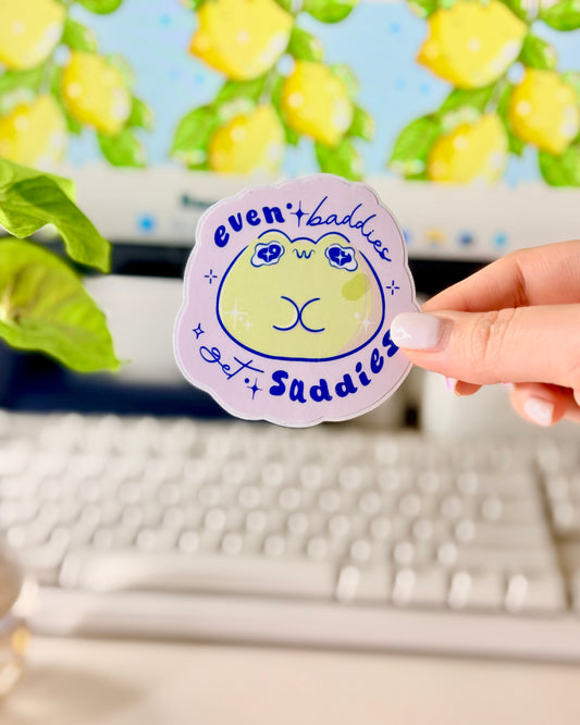 Even Baddies Get Saddies Vinyl Sticker with a cartoon frog character held by a hand in front of a computer screen.