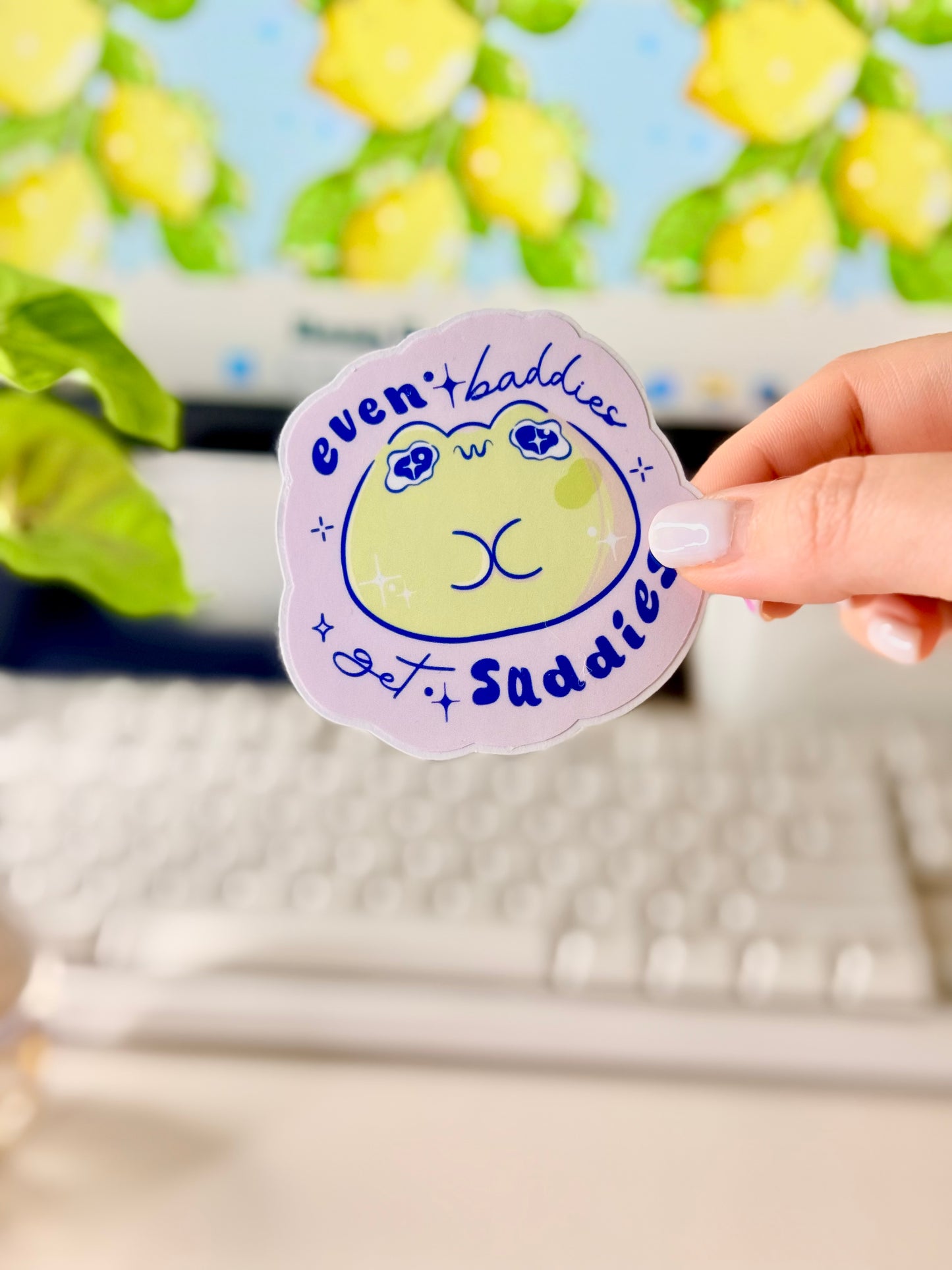 Even Baddies Get Saddies Vinyl Sticker with a cartoon frog character held by a hand in front of a computer screen.