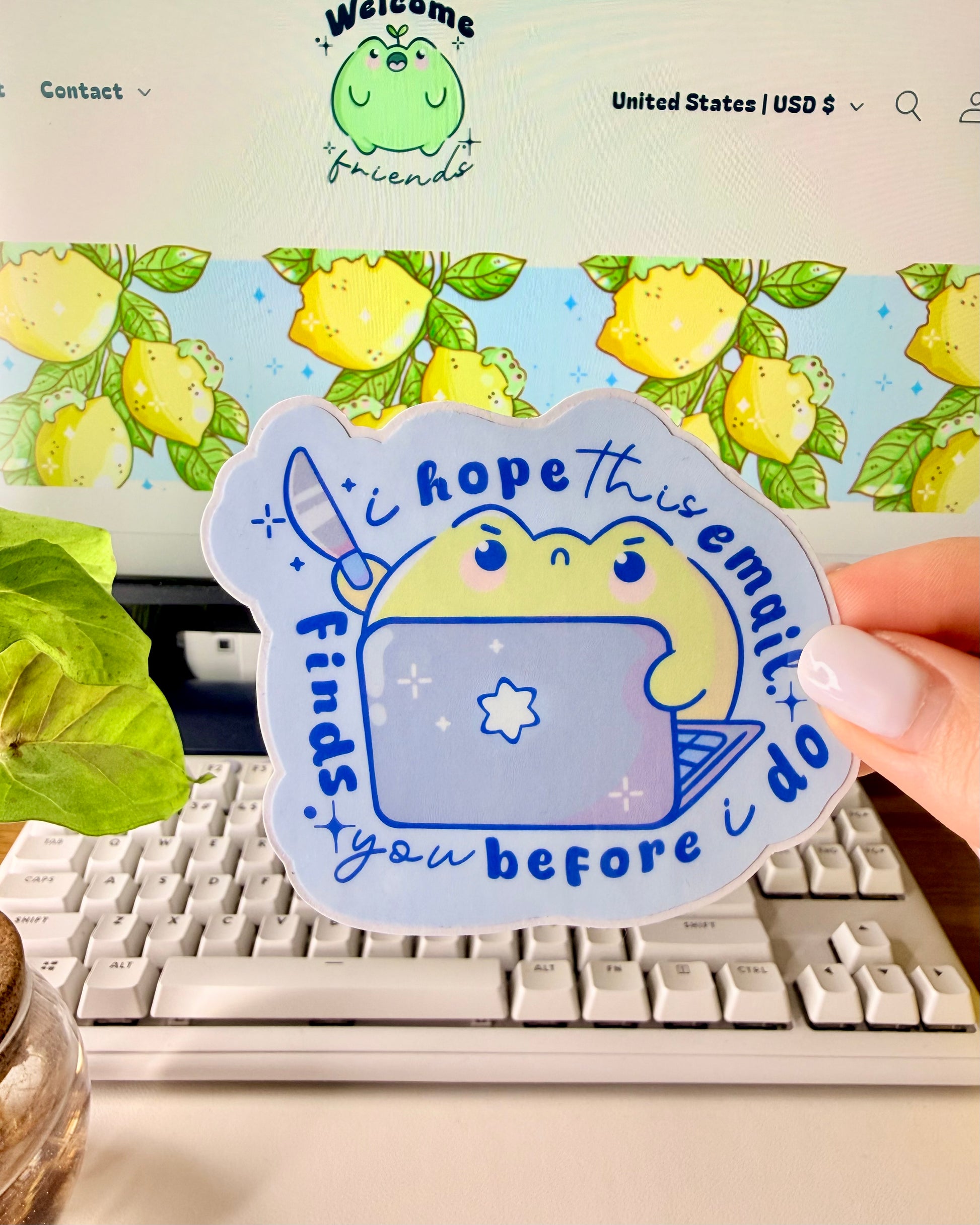 Hand holding a sticker with a cartoon frog character that's holding a knife with the words "I hope this email finds you before I do."