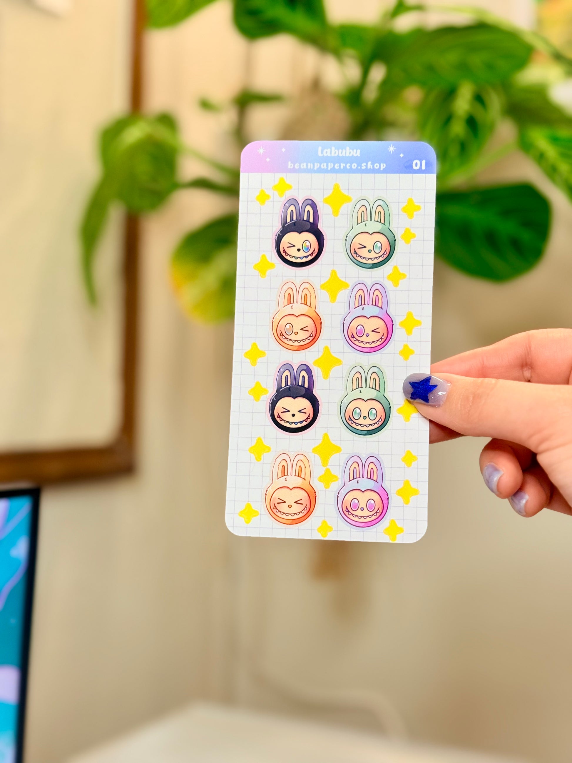 Labubu The Monster Sticker Sheet with black, blue green, orange, and purple labubus held by hand against a blurred background.