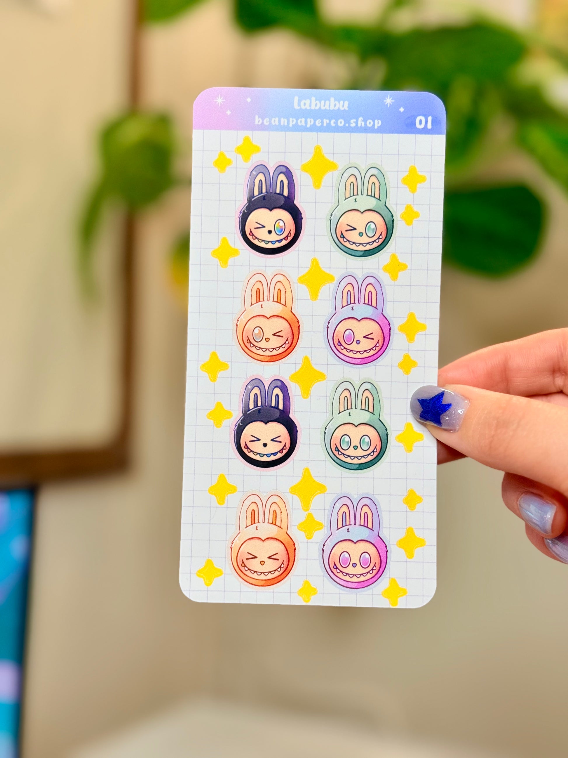 Labubu The Monster Sticker Sheet with black, blue green, orange, and purple labubus held by hand against a blurred background.