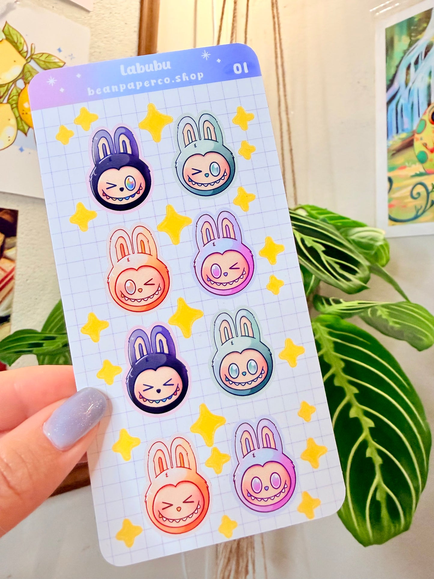 Labubu The Monster Sticker Sheet with black, blue green, orange, and purple labubus held by hand with plant in the background.