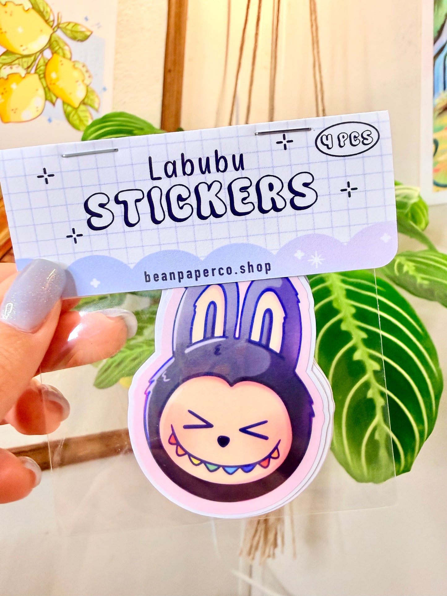 Labubu The Monsters Vinyl Sticker Pack held in hand, with a plant in the background.