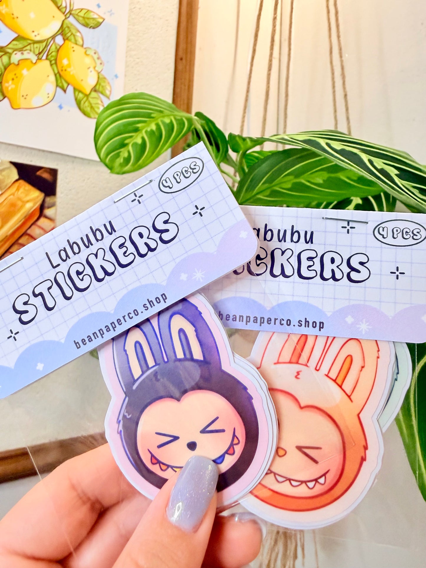 Labubu The Monsters Vinyl Sticker Pack held in hand, with a plant in the background.