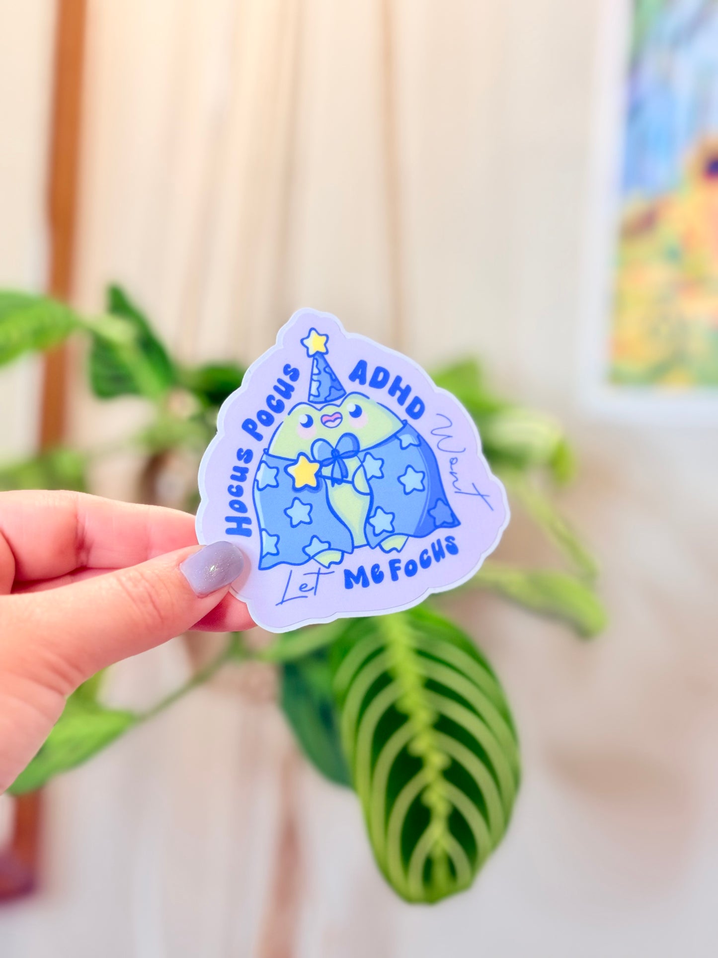 Cute ADHD Focus Frog Sticker Cute Neurodivergent Vinyl Sticker against a background of green plants.
