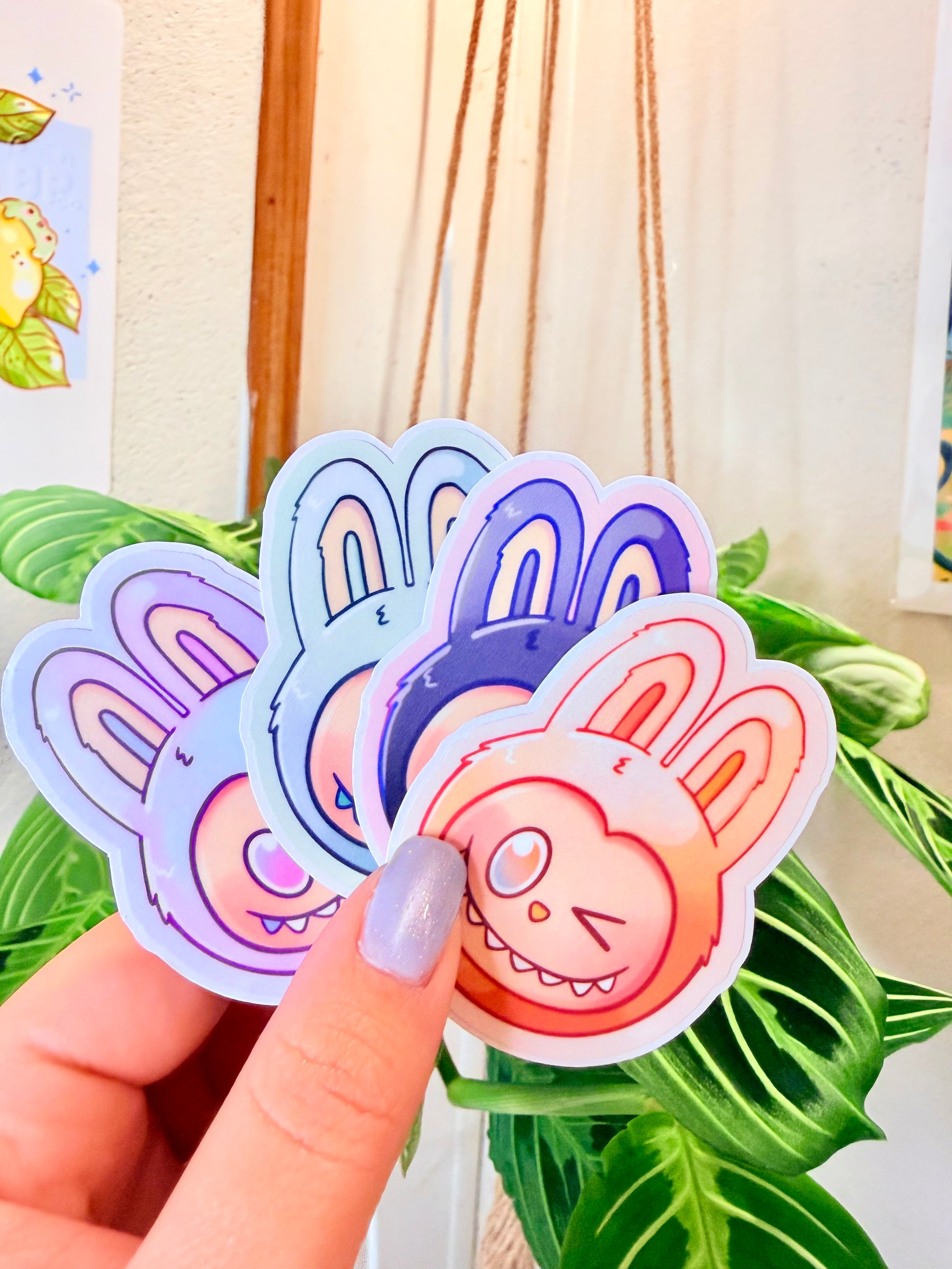 Labubu The Monsters Vinyl Sticker Packs held in hand, with a plant in the background.