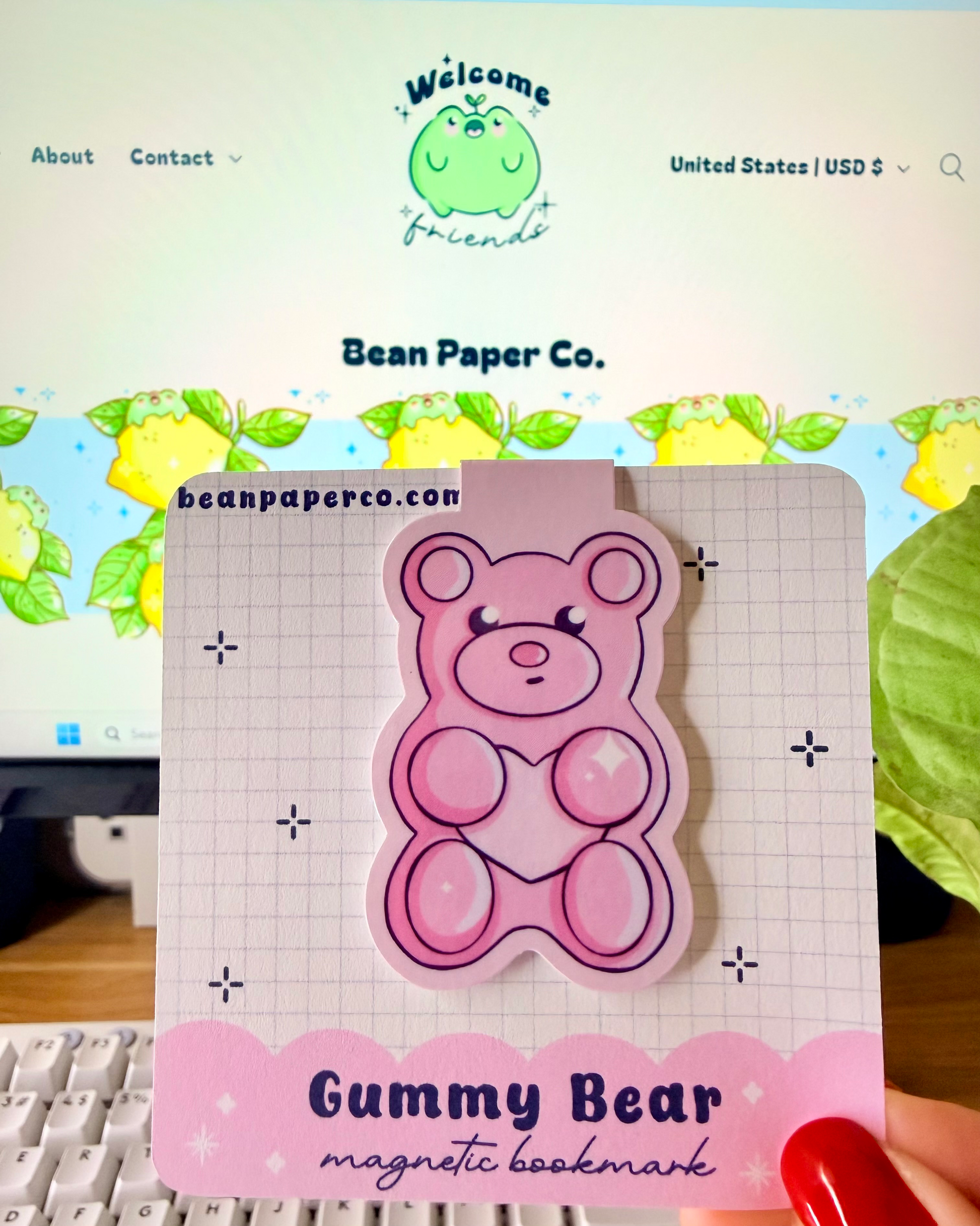 Red & Pink Gummy Bear Magnetic Bookmarks held in hand against blurred Bean Paper Co. website background.