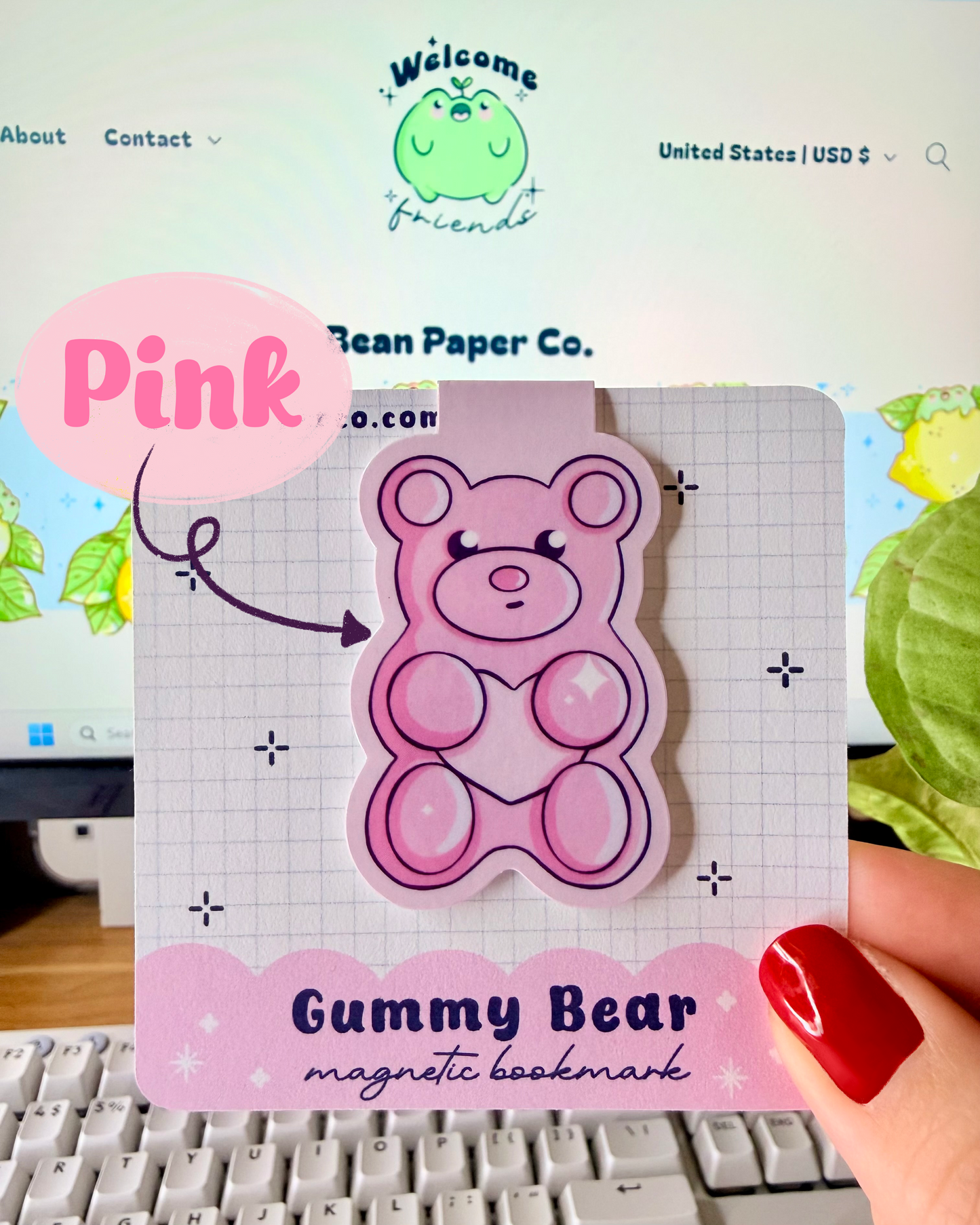 Red & Pink Gummy Bear Magnetic Bookmarks. Pink Magnetic bookmark held in hand against blurred Bean Paper Co. website background.