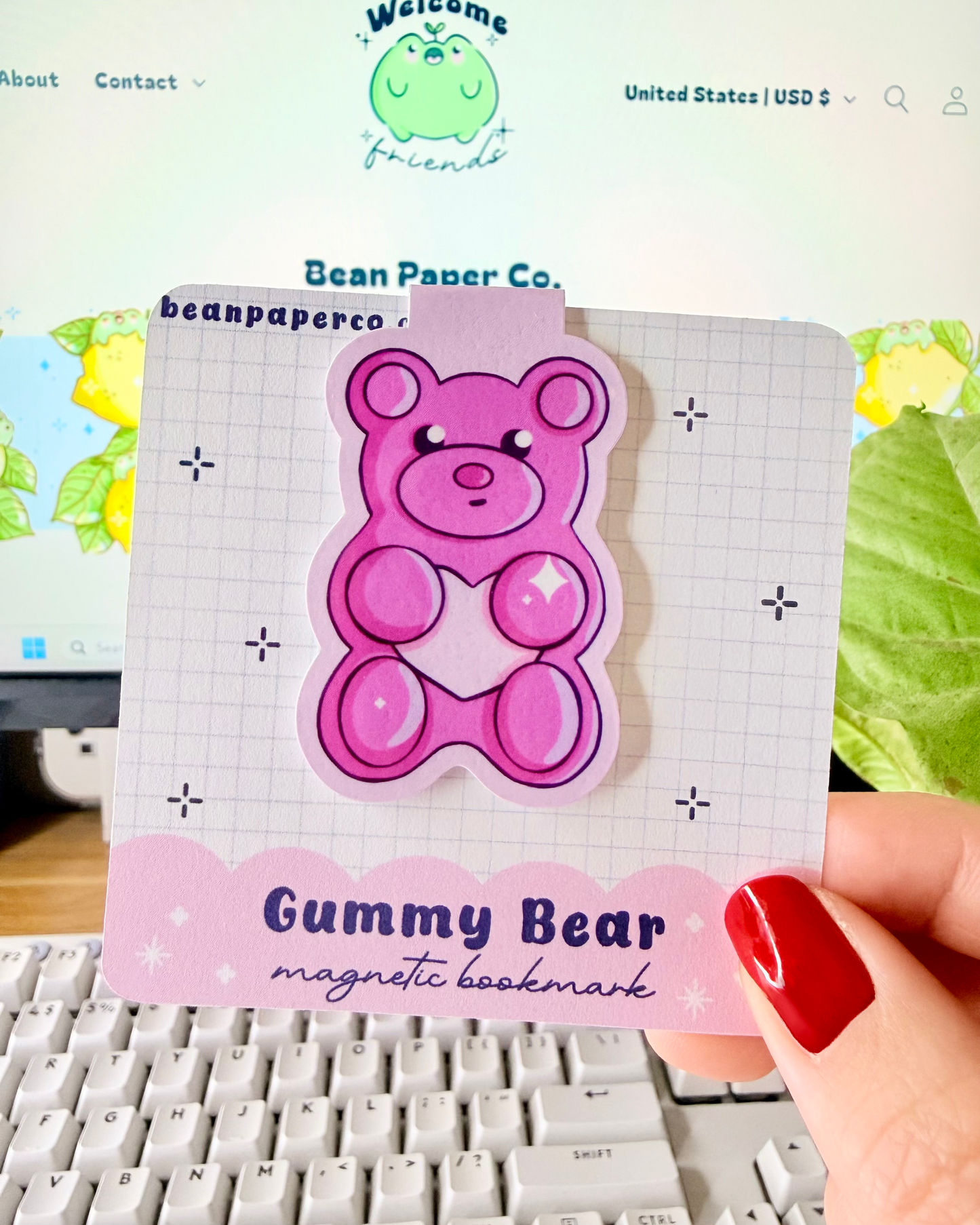 Red & Pink Gummy Bear Magnetic Bookmarks held in hand against blurred Bean Paper Co. website background.