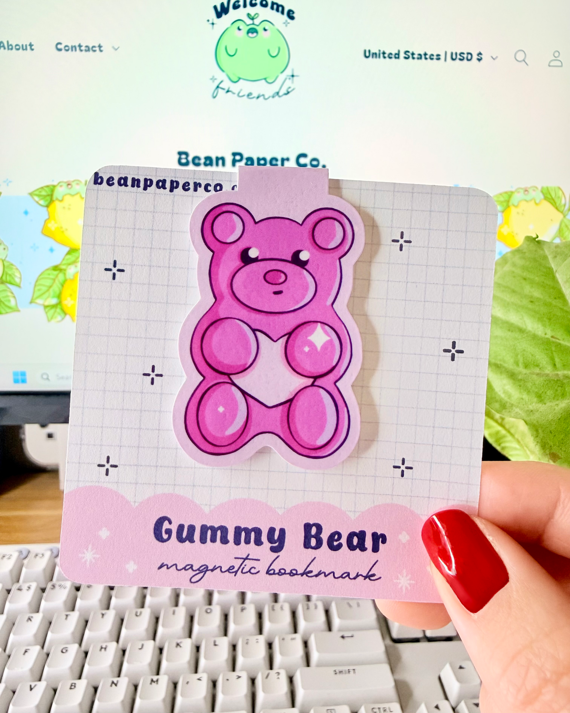Red & Pink Gummy Bear Magnetic Bookmarks held in hand against blurred Bean Paper Co. website background.