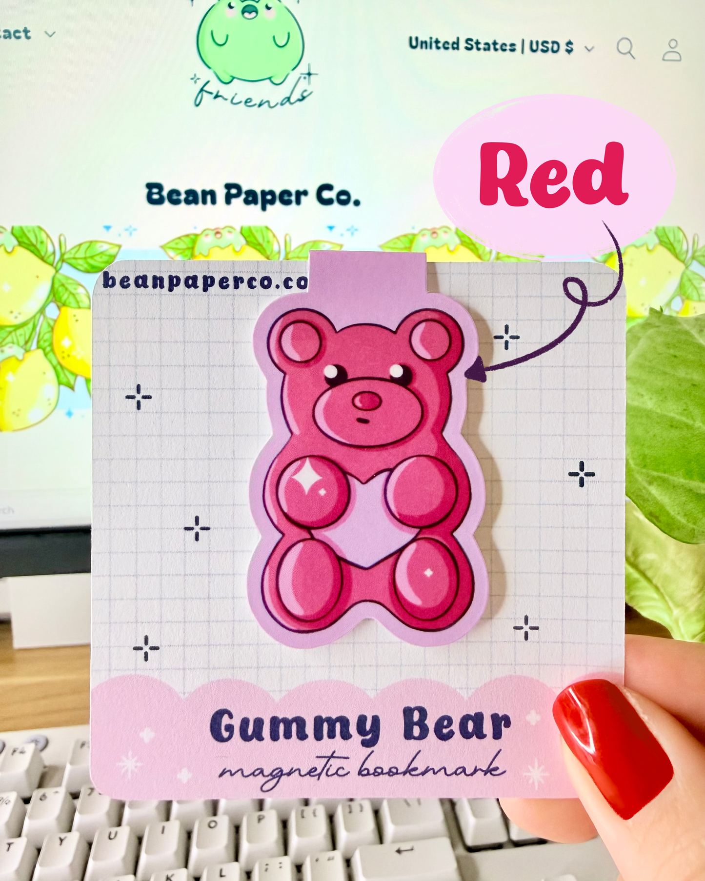 Red & Pink Gummy Bear Magnetic Bookmarks. Red Magnetic bookmark held in hand against blurred Bean Paper Co. website background.