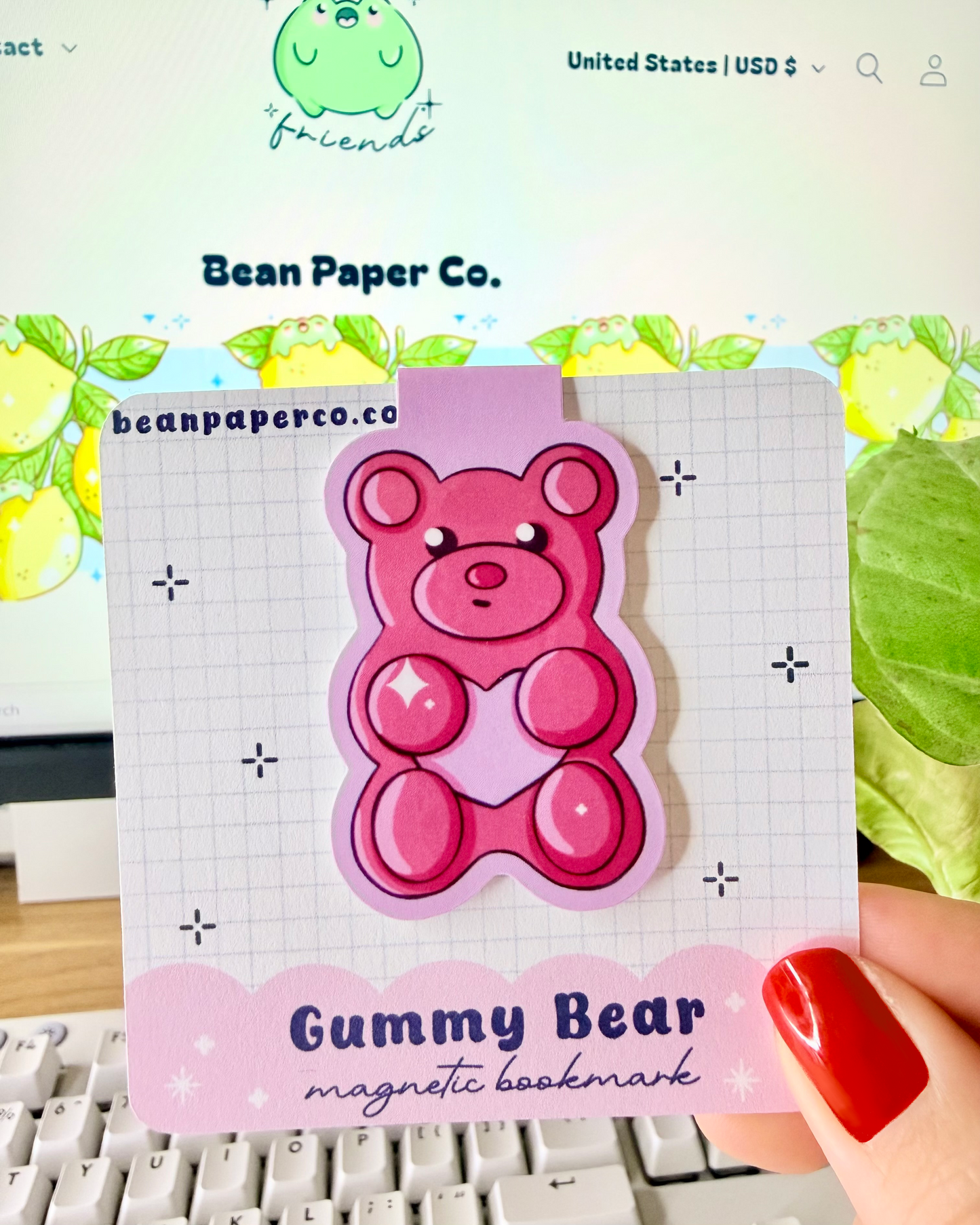 Red & Pink Gummy Bear Magnetic Bookmarks held in hand against blurred Bean Paper Co. website background.