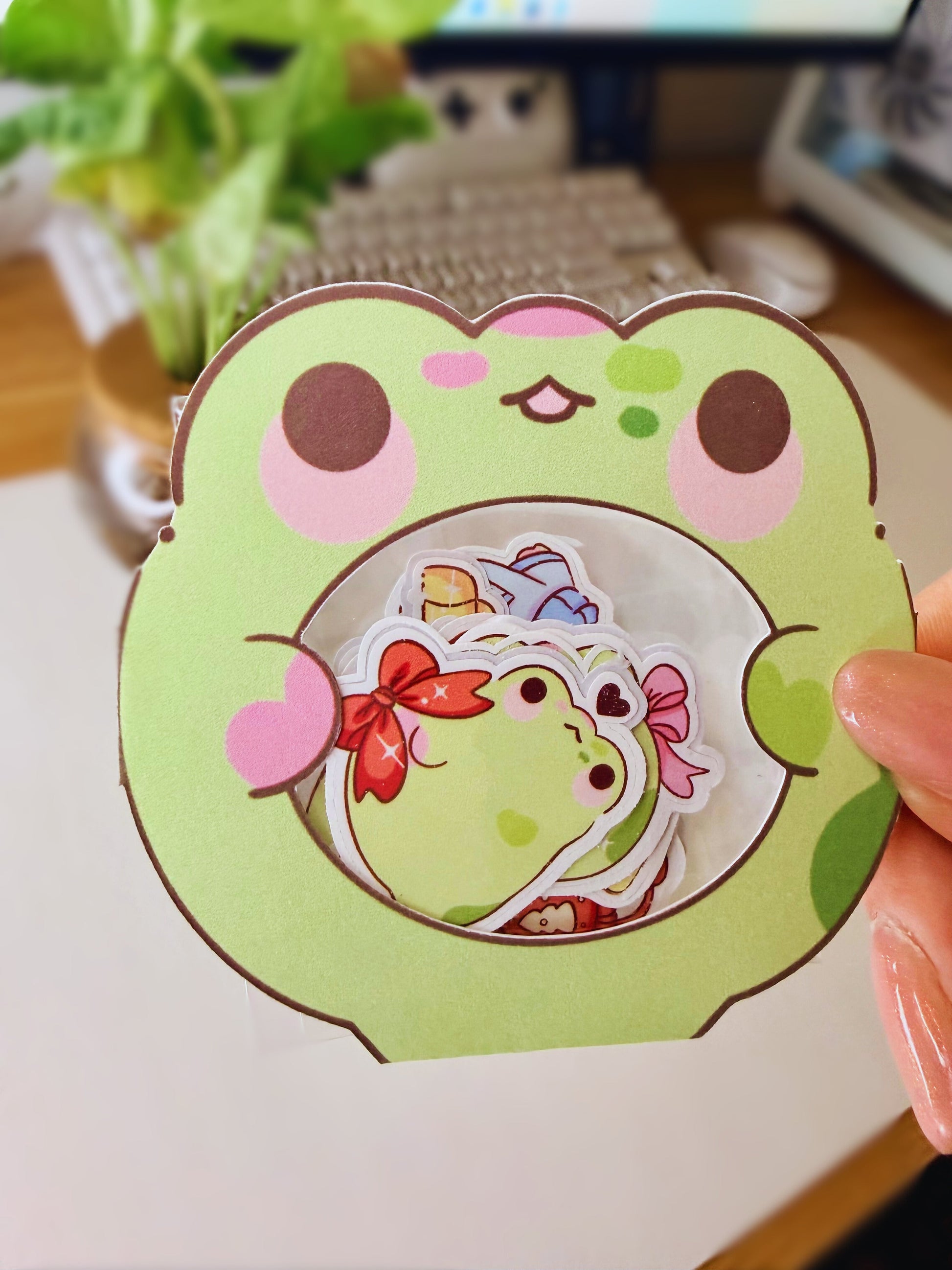 “Frog-shaped packaging holding small die-cut frog sticker flakes on a desk setup.”